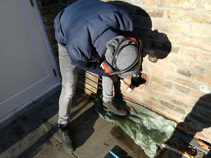 Man bending over using tools on an external wall of a home