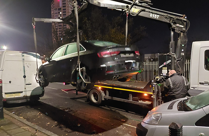 Black car being lifted by crane attached to lorry, to be towed away