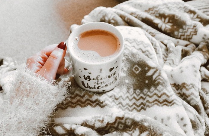 Hand holding a cup of tea with a blanket