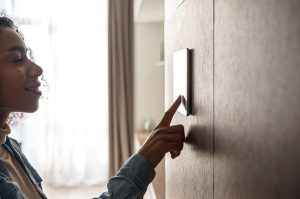 Woman using touch-screen heating system digital control panel on wall in apartment