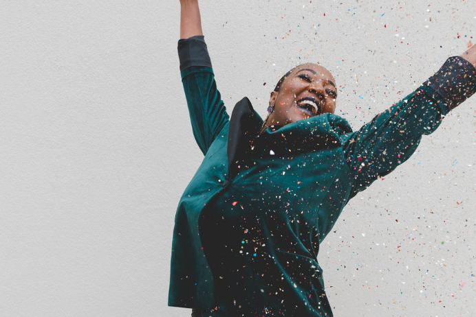 A Black woman laughing among confetti
