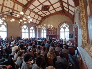 Room full of people sitting on chairs listening to someone speaking