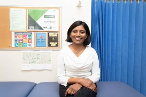 Woman GP sitting on a bench in a surgery office and smiling at the camera