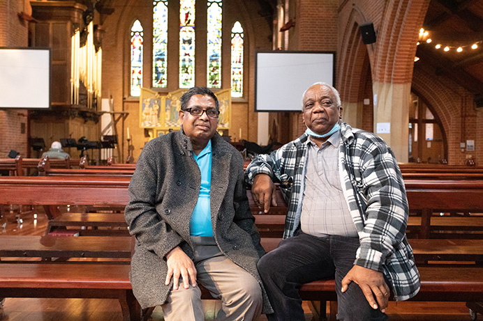 Two men sitting on a church pugh and facing the camera
