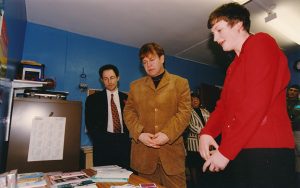 Three people looking at a desk - in the centre is pop star Elton John