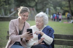 Two women sitting on a bench, one elderly and one younger, looking at a phone