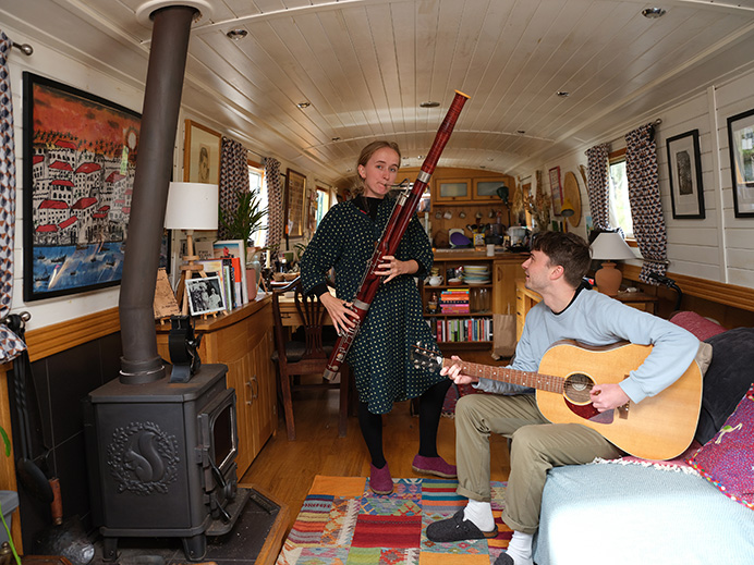 A man holding a guitar and a woman with a bassoon - both inside a canal barge