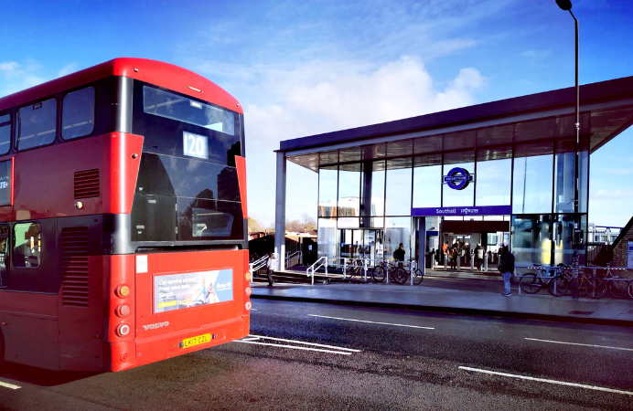 A bus passing by in front of Southall station where there are bikes parked