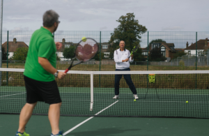 A man in a green t-shirt playing tennis with a man in a white t-shirt