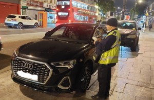 Male officer in high vis vest issuing a fine ticket to a black car.