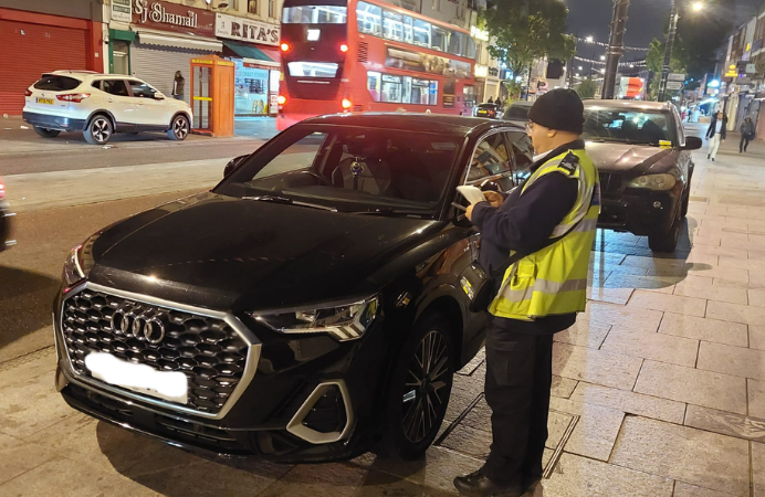 Male officer in high vis vest issuing a fine ticket to a black car.