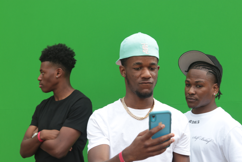 Three black men in front of a green screen, one holding a phone