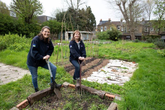 two women in garden leaning on a spade and garden fork