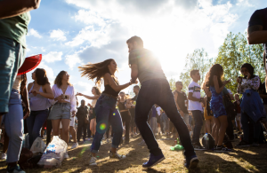 A woman and a man dancing outdoors, surrounded by other people while sun is shining