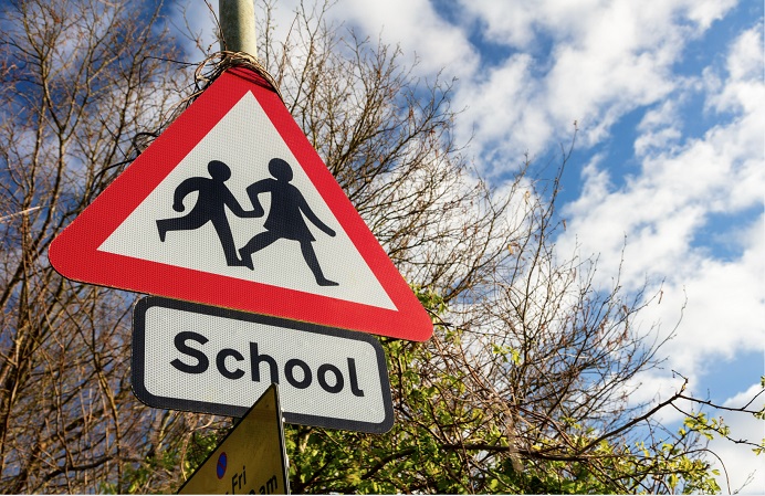 Triangle road sign with two children holding hands and below saying School