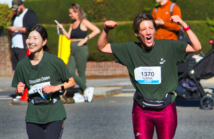 Two women running Ealing Half Marathon, one cheering up with hands in the air