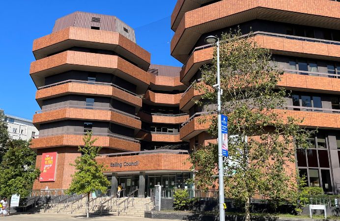 Green trees in front of red brick building with Ealing Council written above the entrance