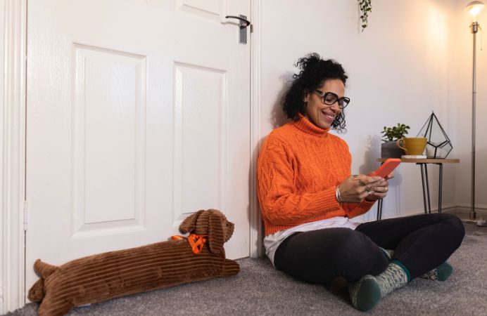Smiling woman sits on floor of flat with draught excluder shaed like dog