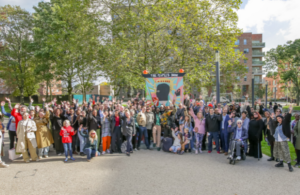 A group of people in front of trees and an arts sculpture smiling and waving