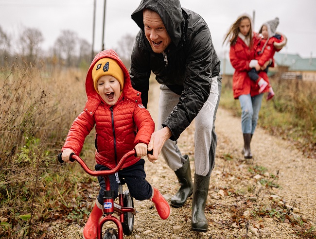 A man pushing a small boy on his bicycle while a woman walks behind them carry a child