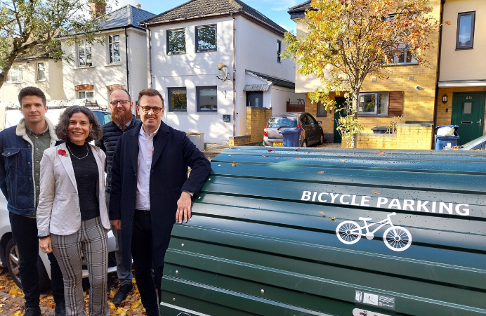 Three men and one woman standing next to a bike hangar and smiling.