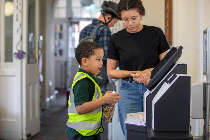 staff member helping child check out a book using the self serve machine at Hanwell Community Library