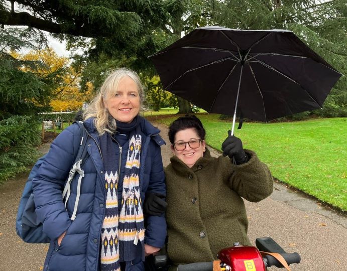 two woman outside, one holding a black umbrella, both smiling