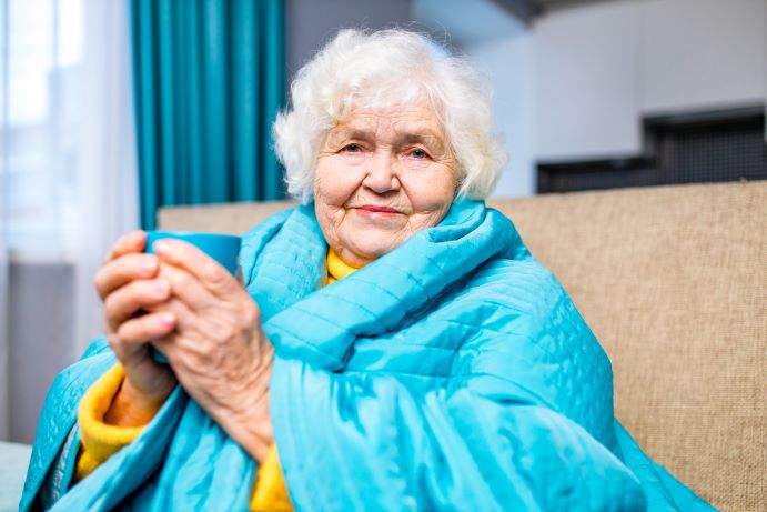 elderly lady holding a mug of tea, wrapped in a blanket