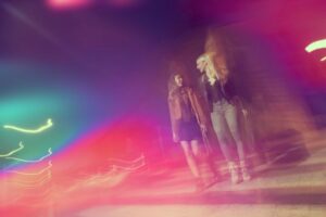 2 girls walking down a street during a night out, with blurred colour effect over picture