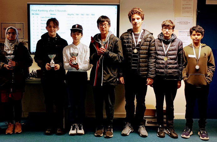 1 girl and 6 boys with trophy's and medals standing in front of a white board