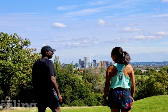 man and woman in running gear standing on a grassy hilltop overlooking London landscape