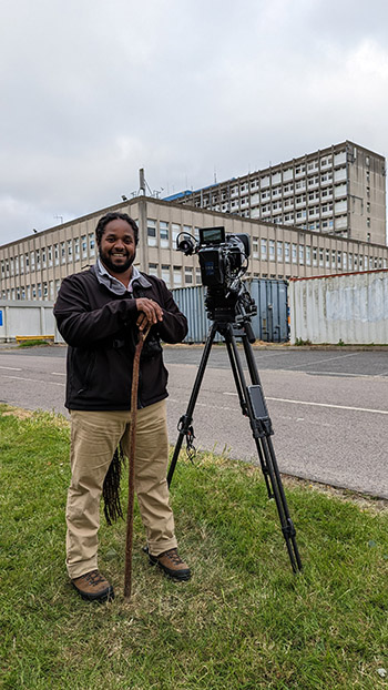 Man standing with camera on tripod near the entrance to Ealing Hospital