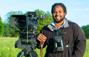 Man standing in field with video camera and smiling