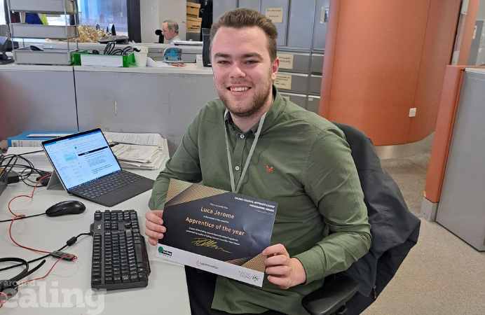 Luca Jerome sitting at his desk, holding his certificate