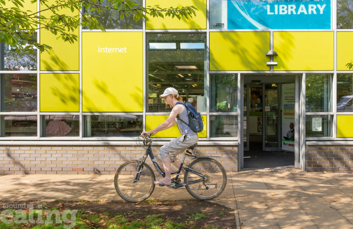A woman on a bike cycling in front of Northolt library.