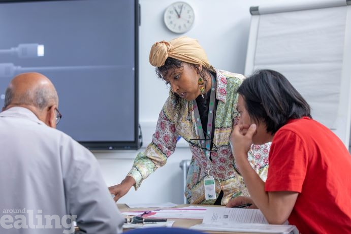 woman leaning over a desk in a classroom with a male and female learner at the desks