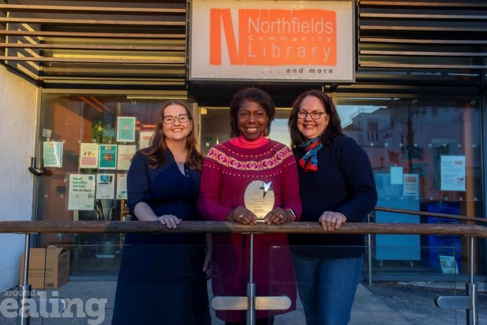 3 female voluteers standing outside the library holding an award