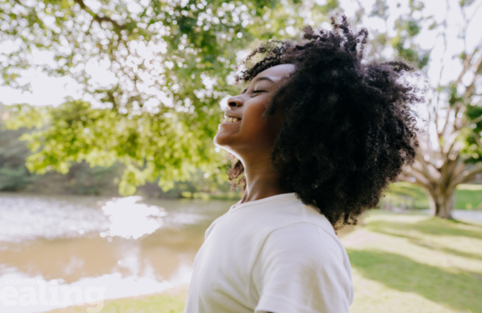 A black woman breathing in fresh air in a park next to a tree