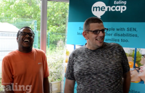 Two men with learning disability in front of an Ealing Mencap sign