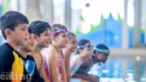 Children sitting on the edge of a swimming pool, looking ahead and smiling