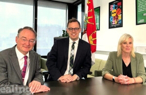 Two men and a woman at a desk smiling at the camera