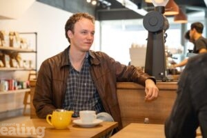 filmmaker Max Mir sitting at a table in West Ealing coffee shop with a cup of coffee