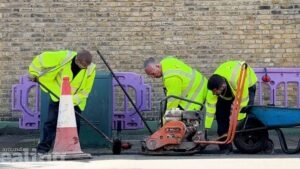 Three men in high-vis jackets bend down to fill a pothole in the road.