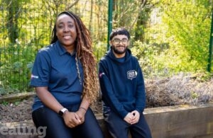 Two people - young woman and man sitting on a wall with trees behind them
