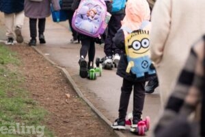 A group of children, wearing colourful backpacks, scooting and walking with their parents to school