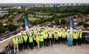 Group of people wearing hard hats and high-vis vests on the roof of a building with a view of houses and green spaces in the distance