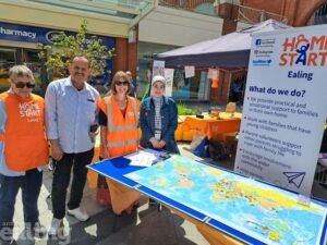 Two men and two women from Home Start Ealing standing beside a table with a map of the world on at Ealing Broadway Shopping Centre to celebrate Refugee Week.