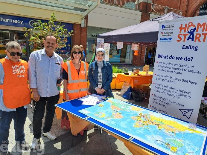 Two men and two women from Home Start Ealing standing beside a table with a map of the world on at Ealing Broadway Shopping Centre to celebrate Refugee Week.