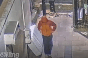 Person wearing red and orange jacket with hood up walking away from a fly-tipped mattress