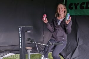 Woman on cyclone works can crushing bike holding two drinks cans
